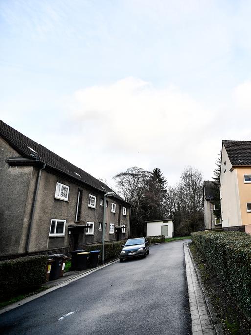 Zweistöckige Mietshäuser stehen an einer Straße, links sind die Häuser grau, rechts gelb gestrichen.