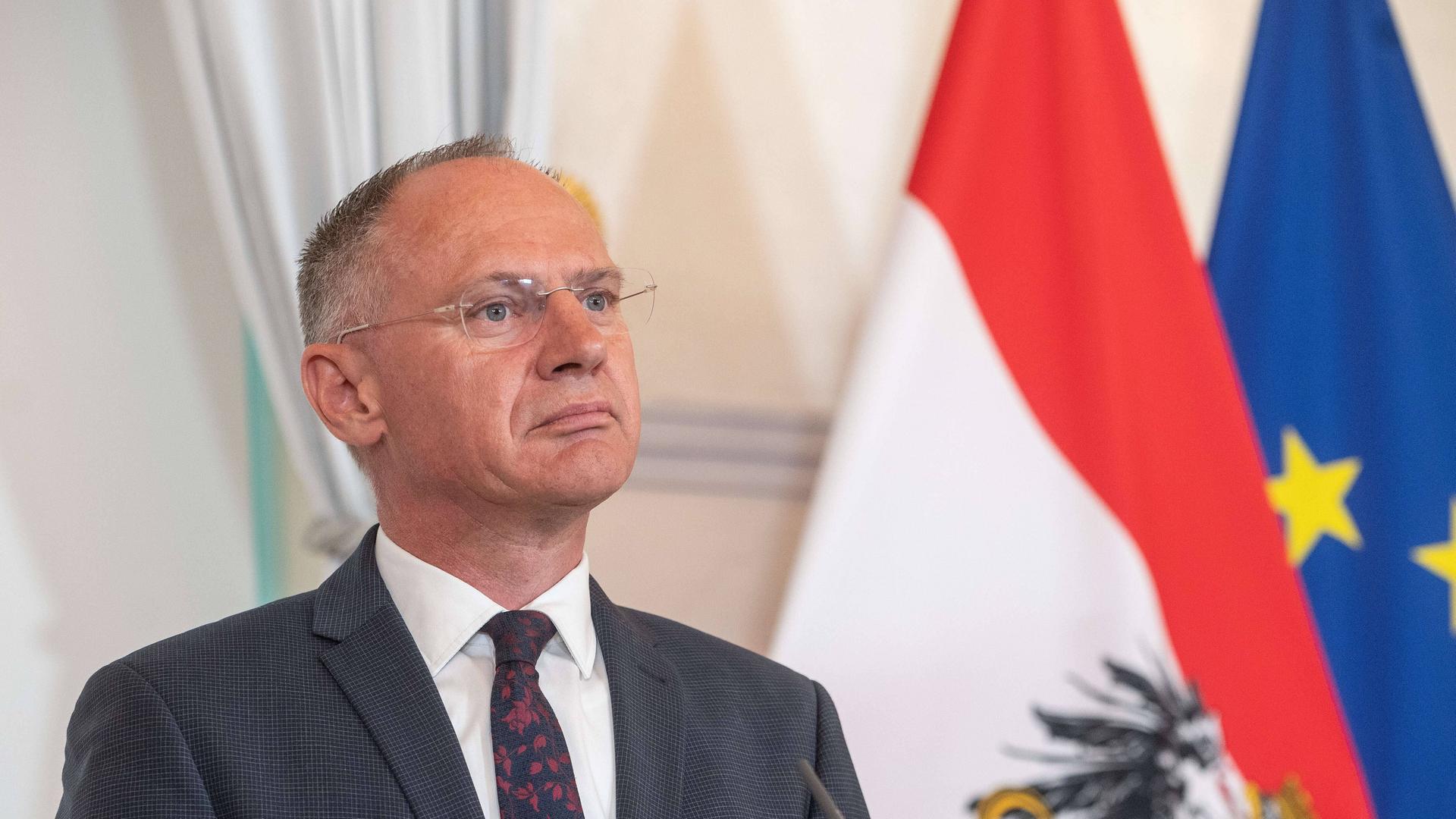 Österreichs Innenminister Gerhard Karner (OEVP) steht vor einer österreichischen- und einer EU-Fahne.