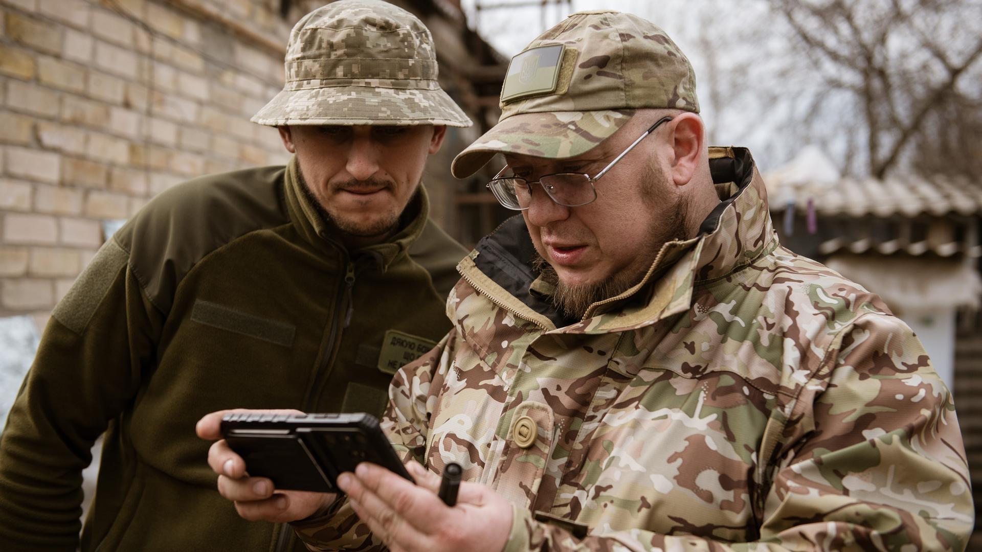 Zwei ukrainische Soldaten betrachten ein Handyvideo von Drohnenangriffen.