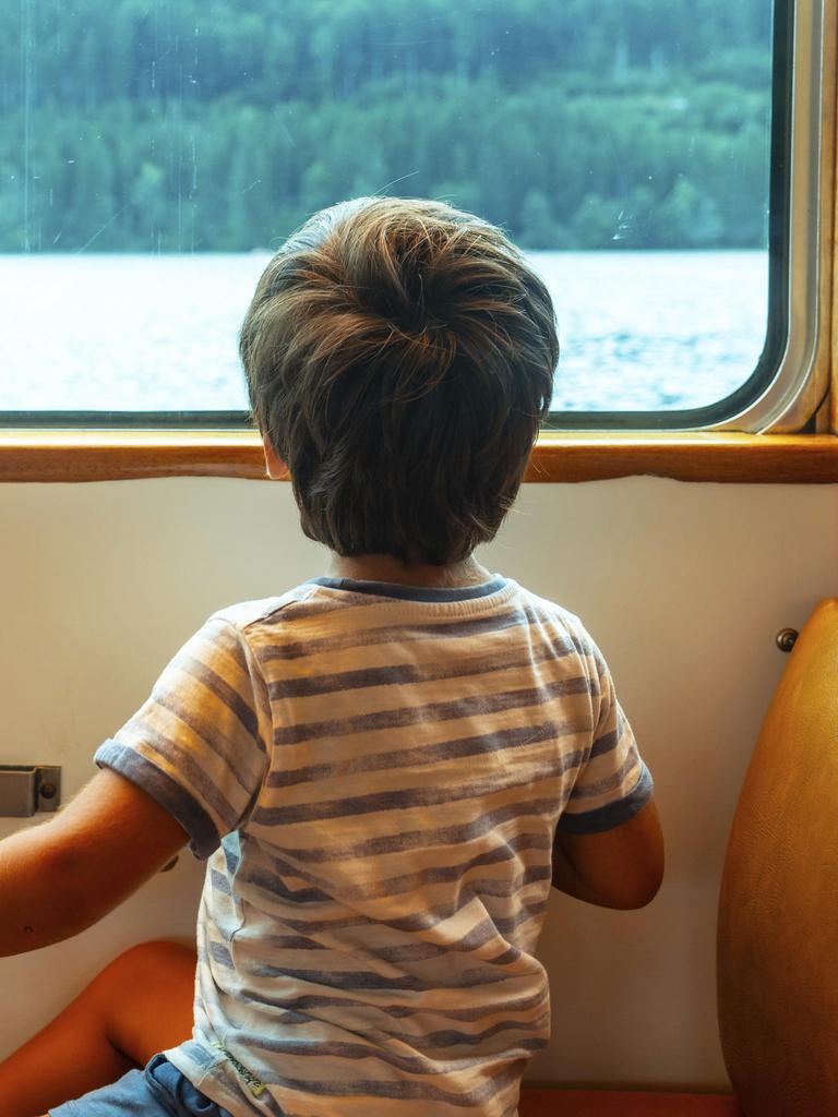 Ein Junge sitzt an einem Zugfenster und schaut auf das Wasser hinaus. Der Junge trägt ein gestreiftes Hemd.