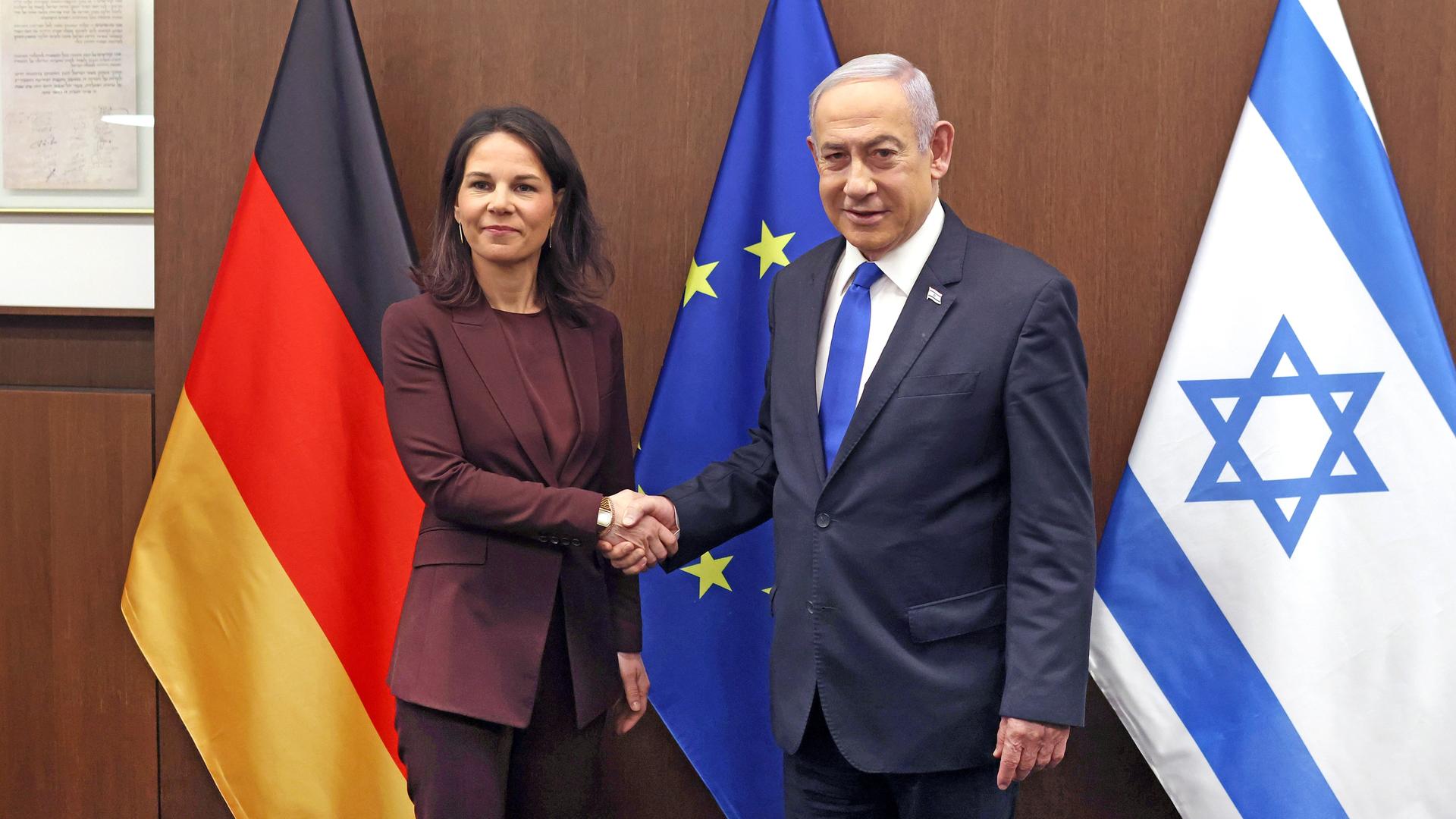 Israels Premierminister Benjamin Netanjahu begrüßt die deutsche Außenministerin Annalena Baerbock. Sie stehen vor Flaggen der EU, Deutschlands und Israel.