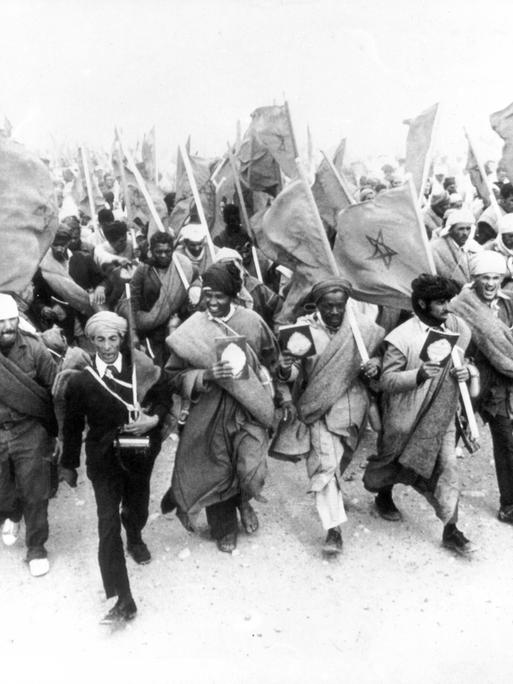 Ein Schwarz-Weiß-Foto zeigt Marokkaner, die mit marokkanischen Nationalflaggen marschieren.