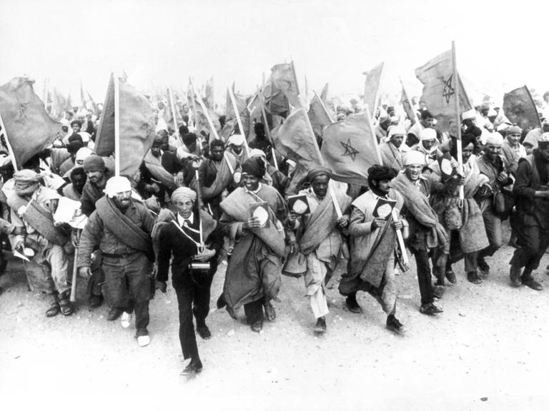 Ein Schwarz-Weiß-Foto zeigt Marokkaner, die mit marokkanischen Nationalflaggen marschieren.