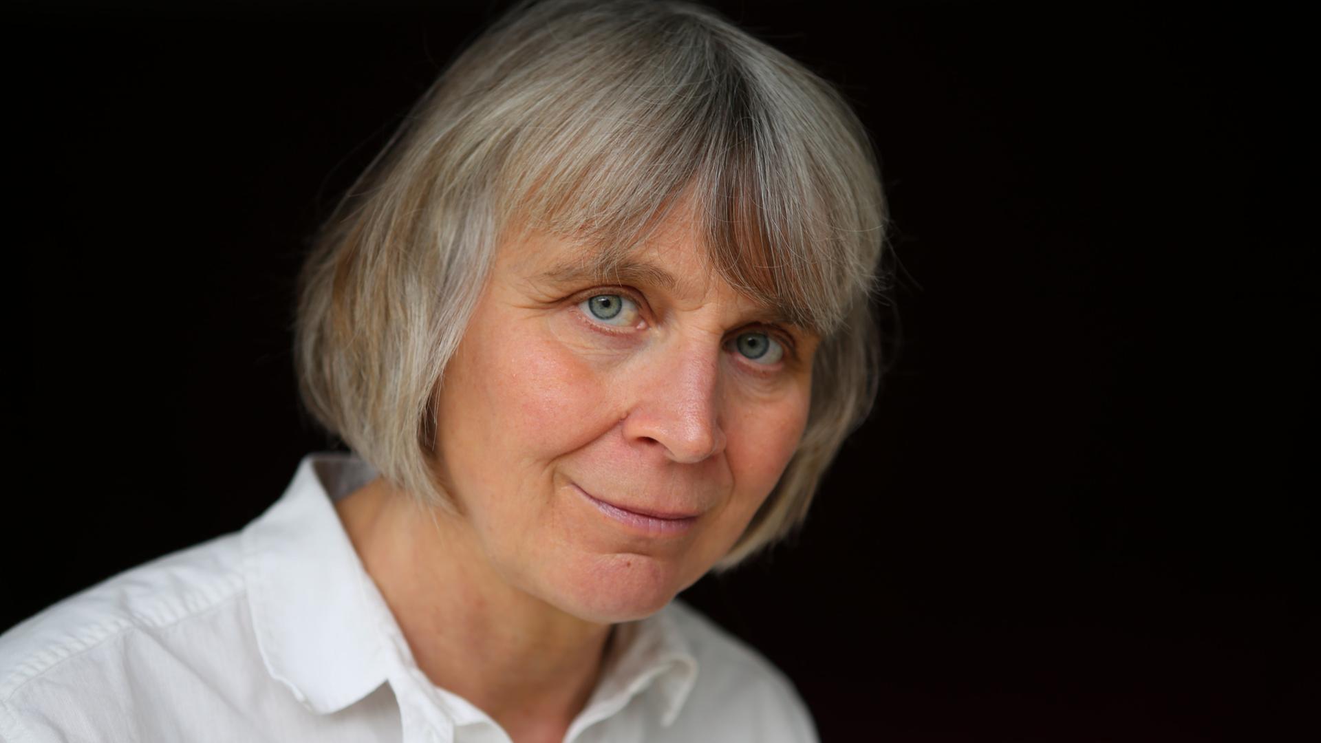 Porträt der Philosophin Barbara Schmitz. Sie trägt kutze, graue Haare und eine weiße Bluse vor schwarzem Hintergrund. Porträt der Philosophin Barbara Schmitz. Sie trägt kutze, graue Haare und eine weiße Bluse vor schwarzem Hintergrund.