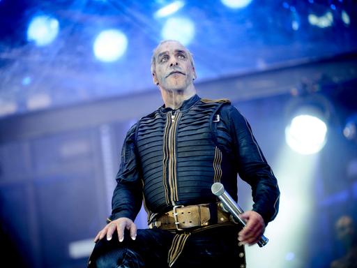 Till Lindemann, Sänger der Band Rammstein, auf der Bühne mit einem schwarz-gelben Kostüm. Im Hintergrund unscharf Scheinwerfer und blaues Licht.