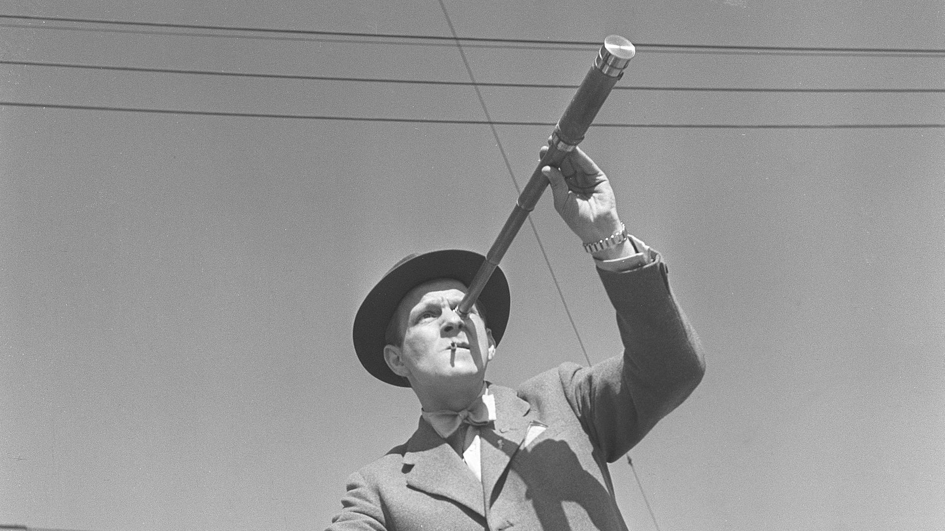 Schwarz-Weiß-Foto aus den1940er-Jahren: Ein Mann auf einem Fahrrad betrachtet etwas durch ein Fernrohr. 