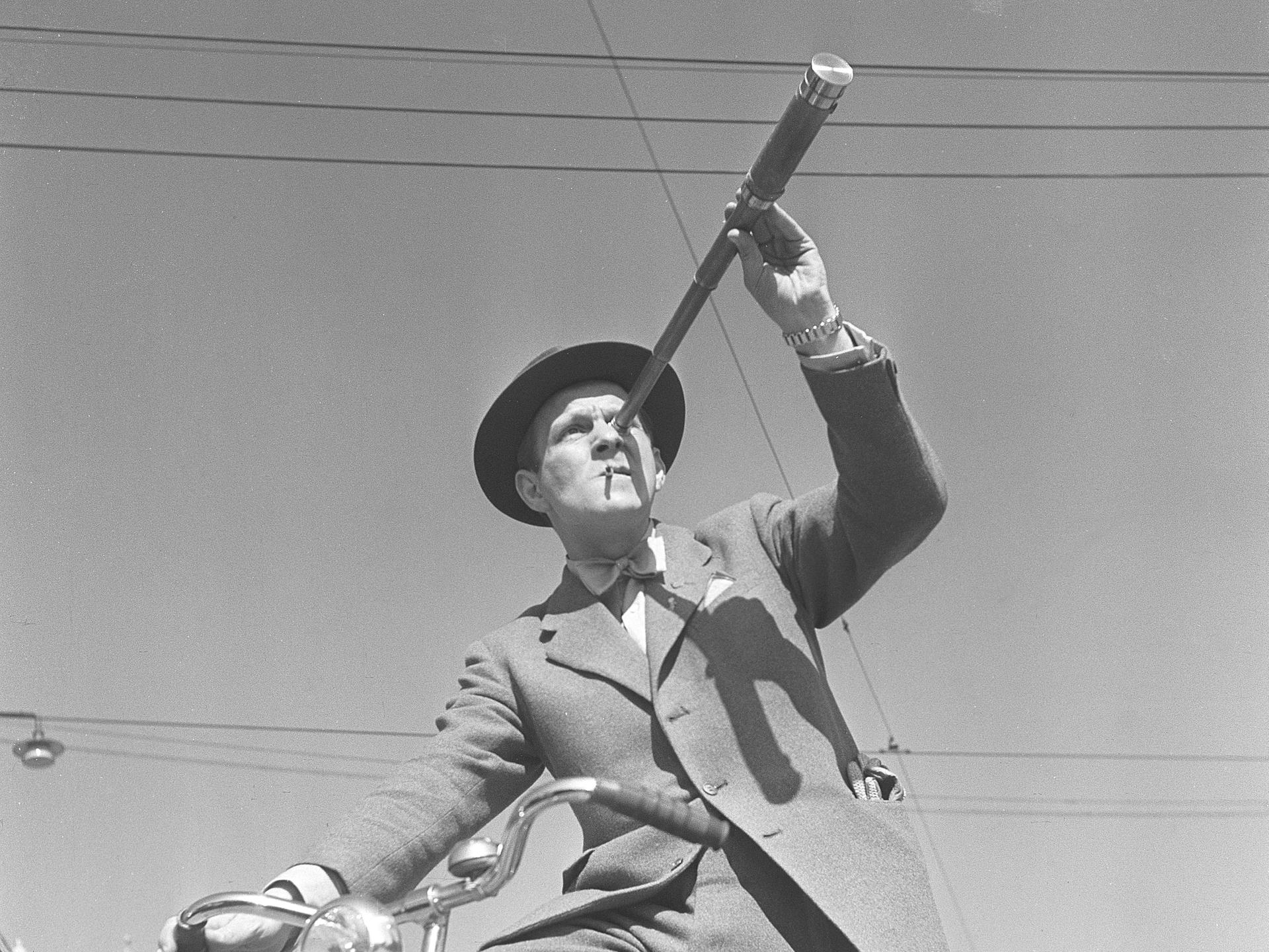 Schwarz-Weiß-Foto aus den1940er-Jahren: Ein Mann auf einem Fahrrad betrachtet etwas durch ein Fernrohr. 