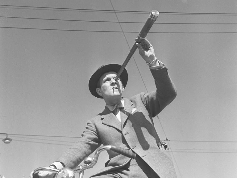 Schwarz-Weiß-Foto aus den1940er-Jahren: Ein Mann auf einem Fahrrad betrachtet etwas durch ein Fernrohr. 
