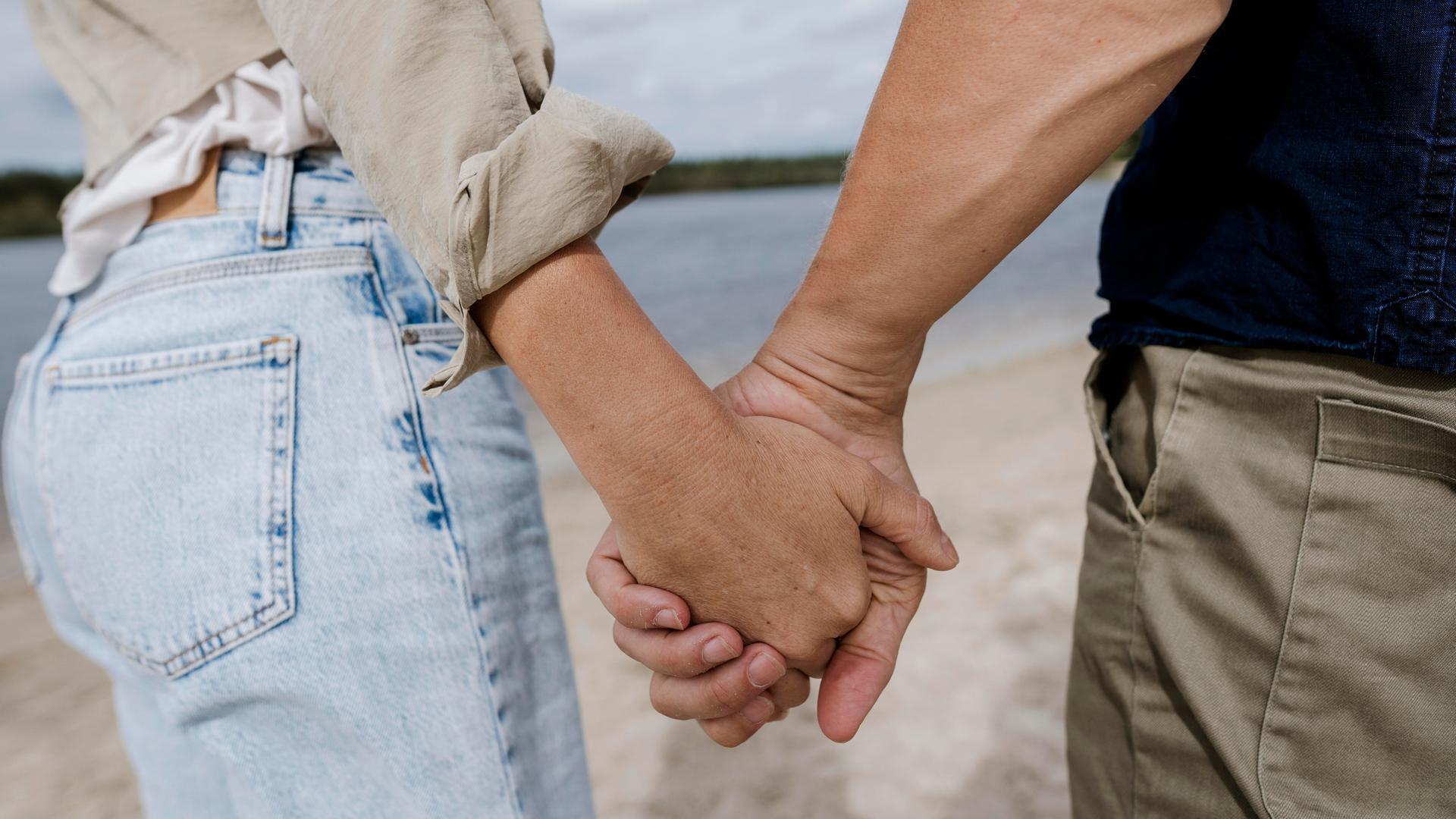 Ein Pärchen hält Händchen am Strand.