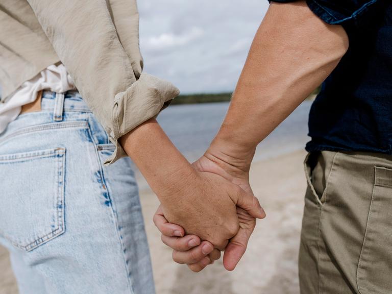 Ein Pärchen hält Händchen am Strand.