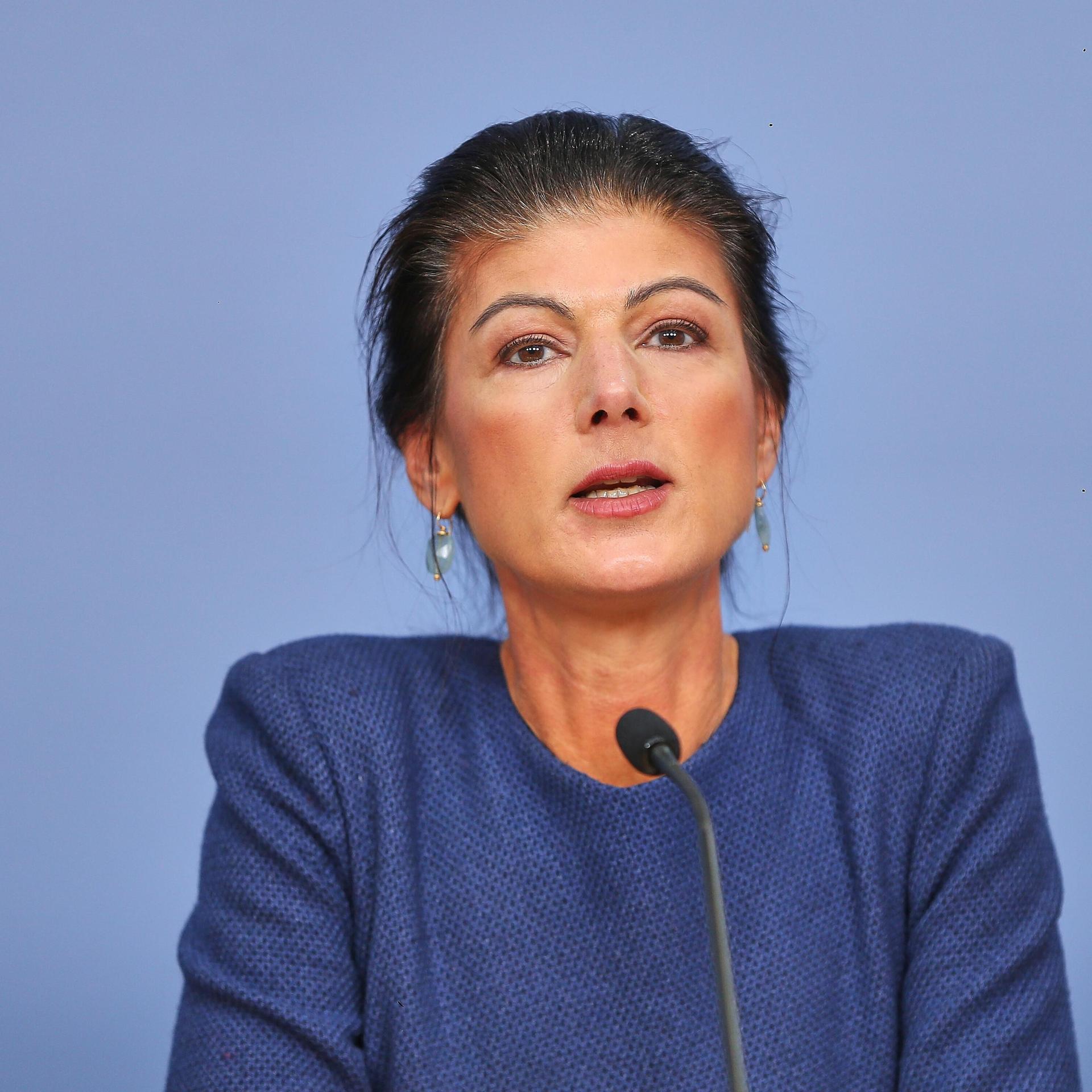 Sahra Wagenknecht sitzt bei einer Pressekonferenz in Berlin vor einem blauen Hintergrund.