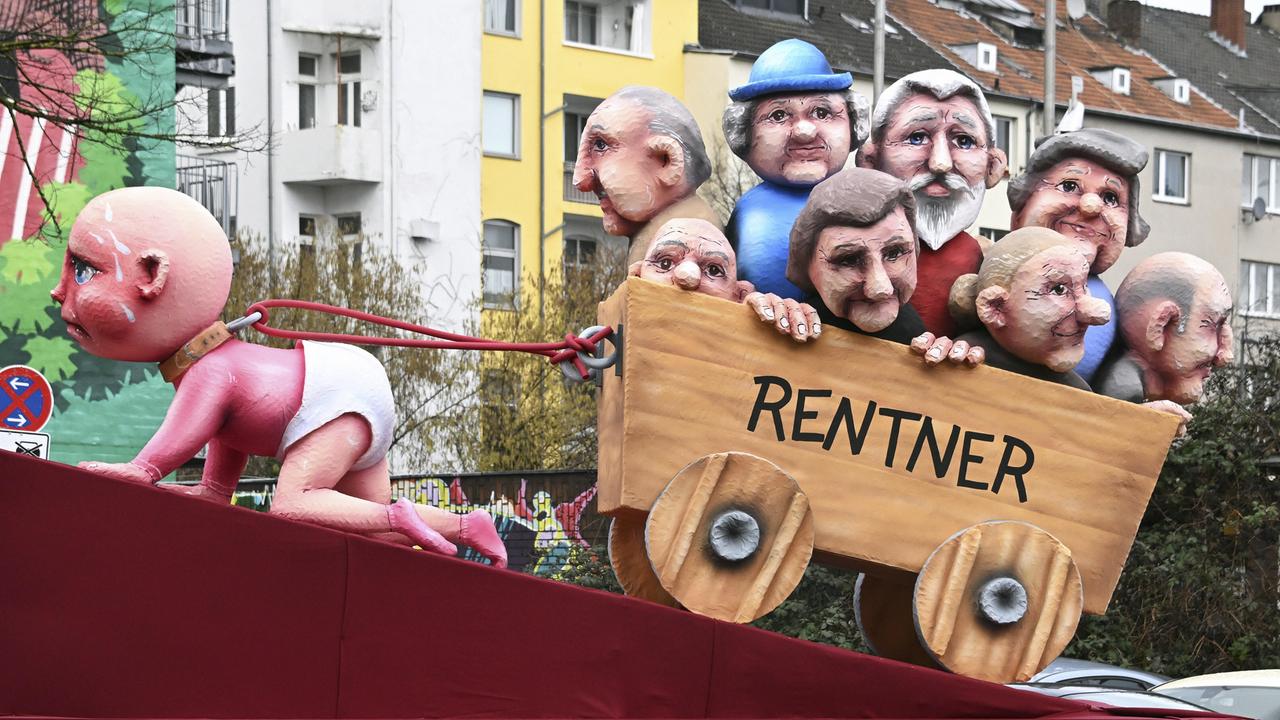 Rosenmontagszug in Düsseldorf: ein Themenwagen zeigt ein Baby, das mühevoll einen Karren mit Rentnern zieht.