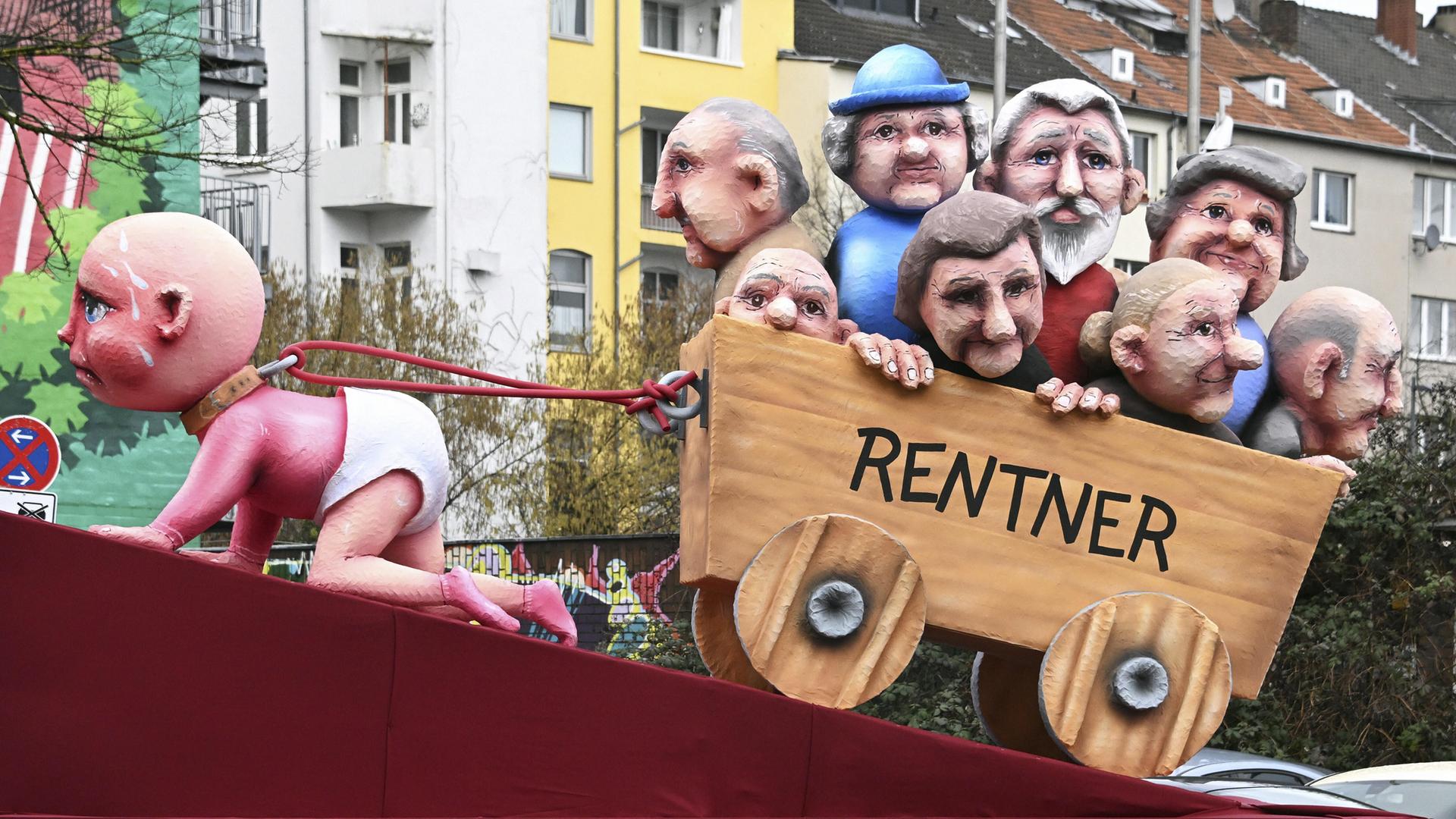 Rosenmontagszug in Düsseldorf: ein Themenwagen zeigt ein Baby, das mühevoll einen Karren mit Rentnern zieht.