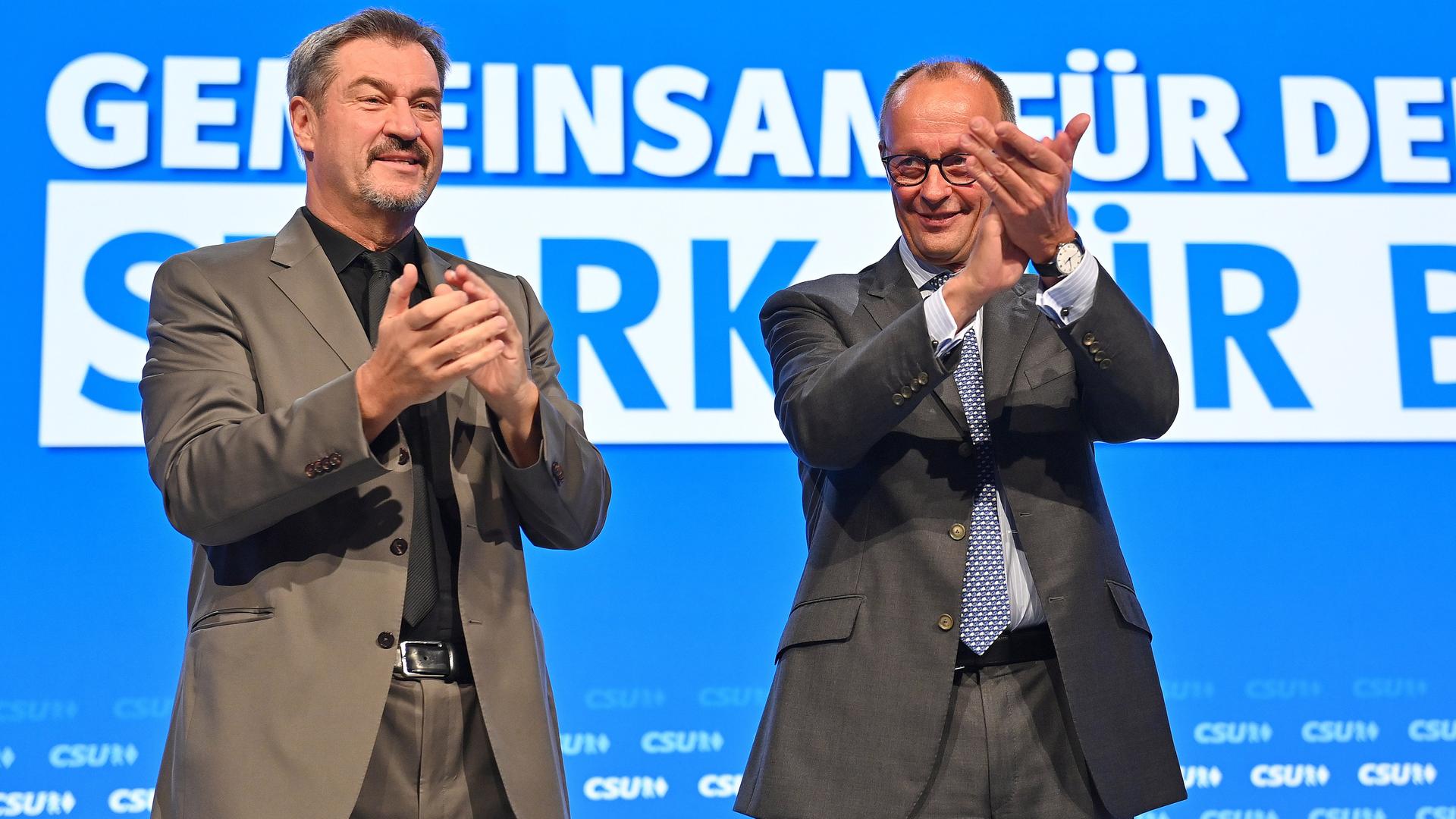 CSU-Parteichef Markus Söder und CDU-Parteichef Friedrich Merz stehen auf einer Bühne während des CSU-Parteitags und klatschen in die Hände.