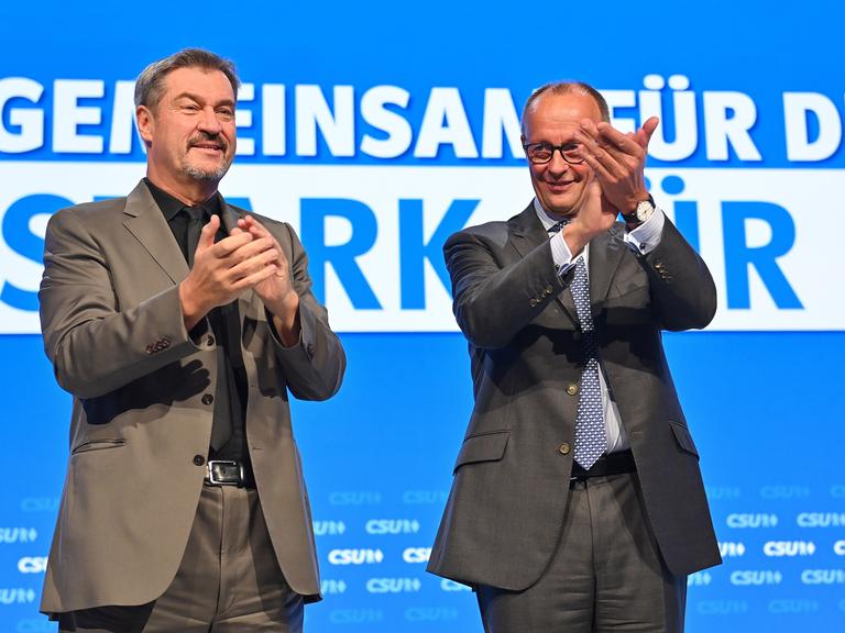 CSU-Parteichef Markus Söder und CDU-Parteichef Friedrich Merz stehen auf einer Bühne während des CSU-Parteitags und klatschen in die Hände.