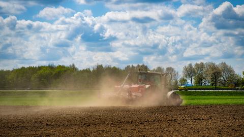 Ein Landwirt beim Eggen seines staubtrockenen Ackers. Wegen der Trockenheit zieht er eine große Staubwolke hinter sich her.