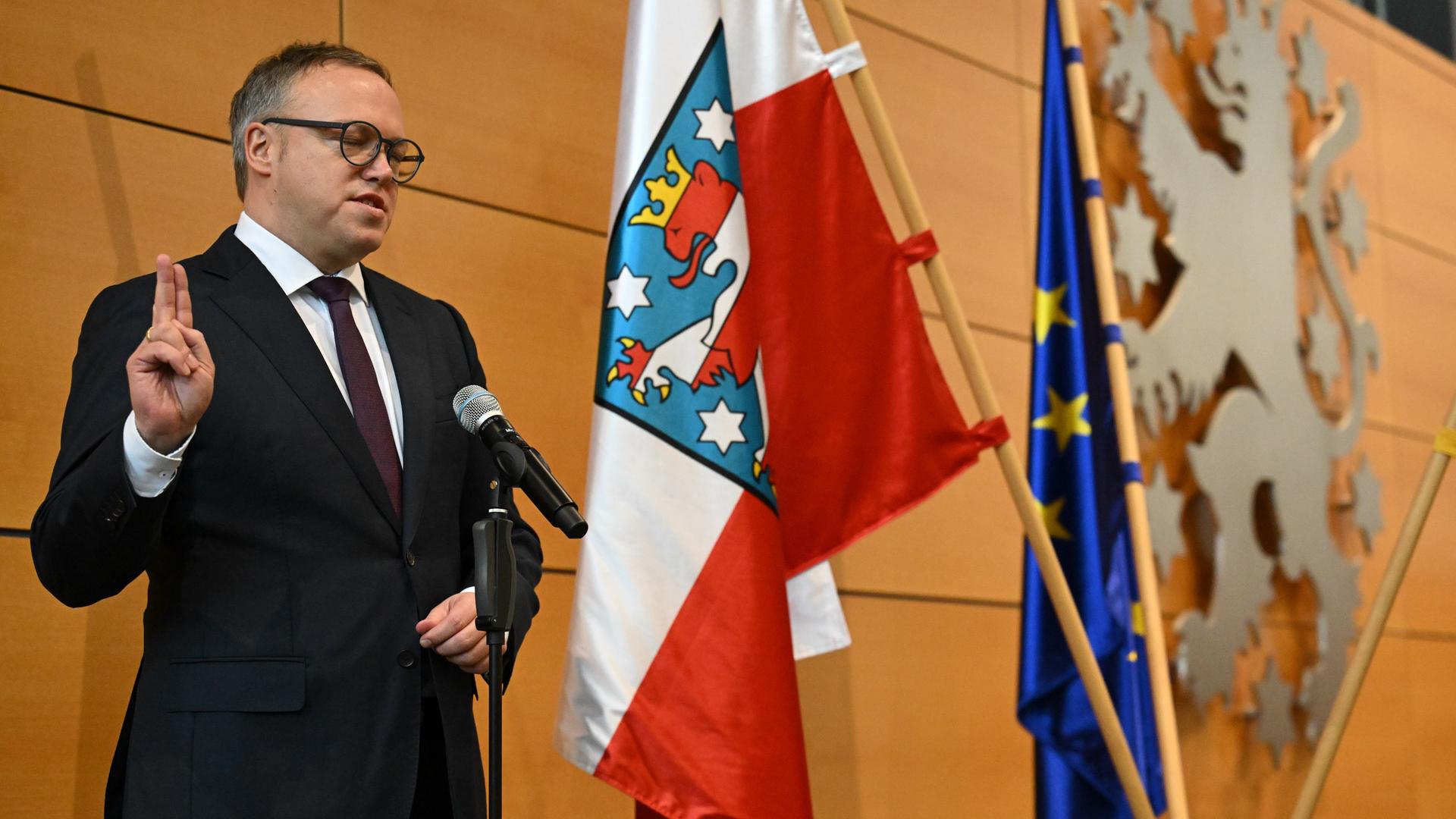 Mario Voigt wird als neuer Minister-Präsident vereidigt. Er hebt die Hand zum Eid. Hinter ihm ist die Fahne von Thüringen zu sehen. 