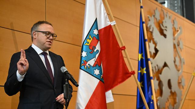 Mario Voigt wird als neuer Minister-Präsident vereidigt. Er hebt die Hand zum Eid. Hinter ihm ist die Fahne von Thüringen zu sehen. 