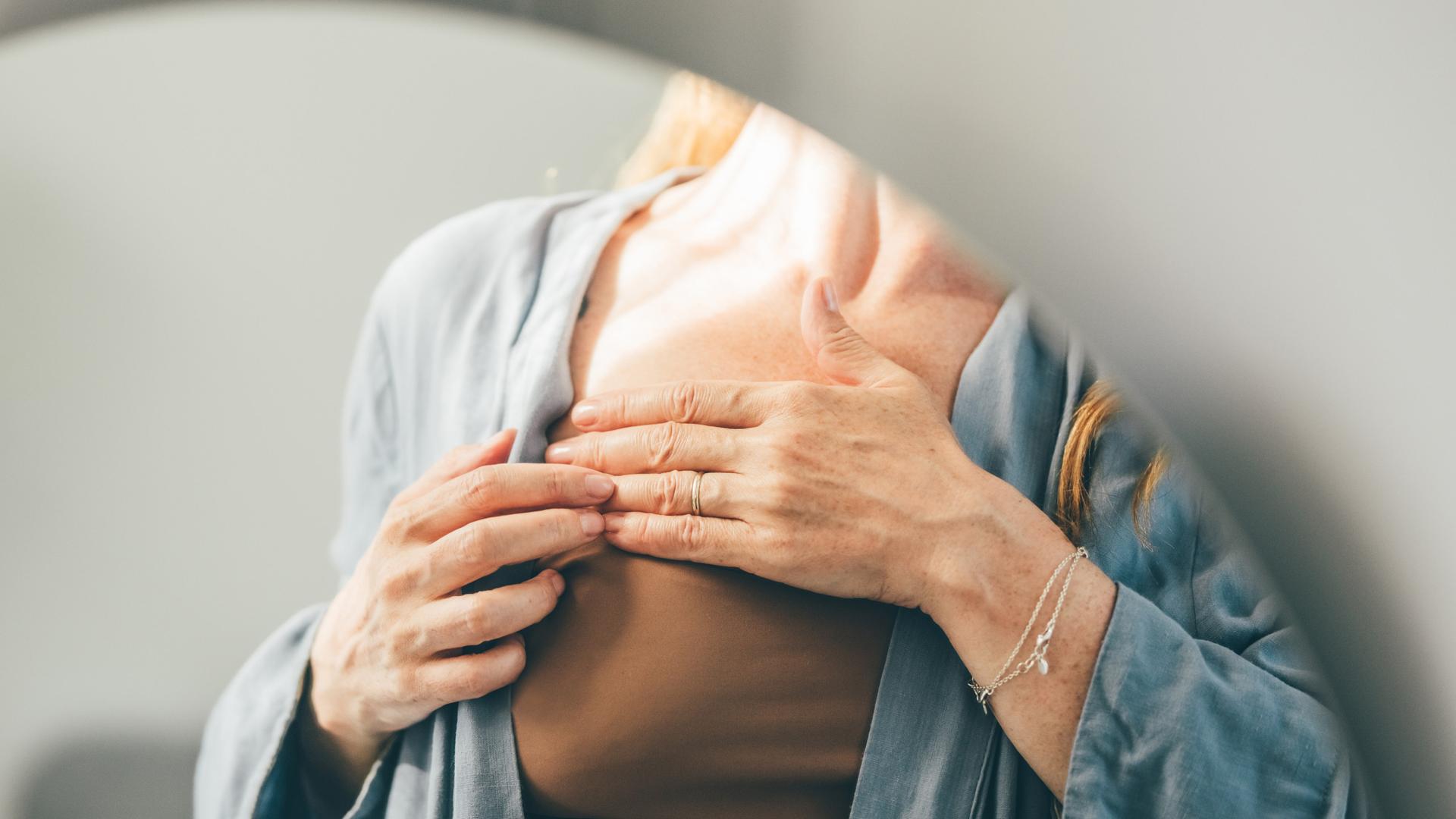 Ausschnitt einer Frau im Spiegel, die ihre Brust abtastet, um auf Krebs aufmerksam zu machen. Ausschnitt einer Frau im Spiegel, die ihre Brust abtastet, um auf Krebs aufmerksam zu machen.