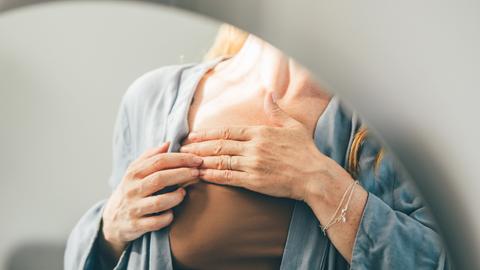 Ausschnitt einer Frau im Spiegel, die ihre Brust abtastet, um auf Krebs aufmerksam zu machen.