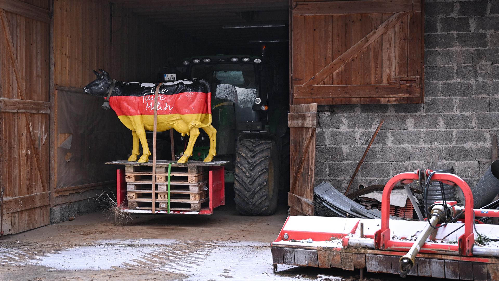 Auf einem Bauernhof in einer Halle steht die Figur einer Kuh; sie ist schwarz, rot, gelb angemalt, mit der Aufschrift "Die faire Milch"