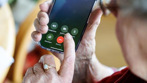 Der Finger einer Seniorin schwebt über einem roten Knopf auf einem Smartphone