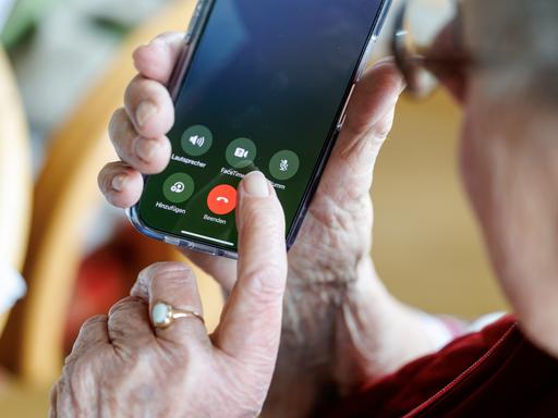 Der Finger einer Seniorin schwebt über einem roten Knopf auf einem Smartphone