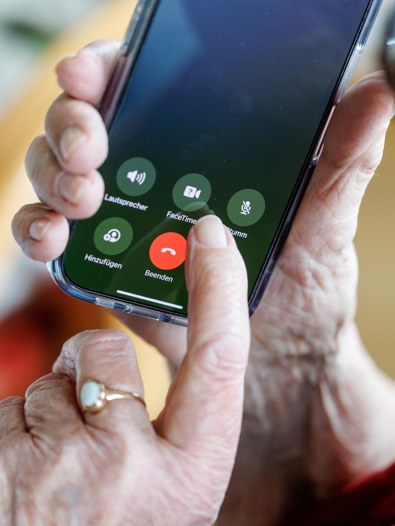 Der Finger einer Seniorin schwebt über einem roten Knopf auf einem Smartphone