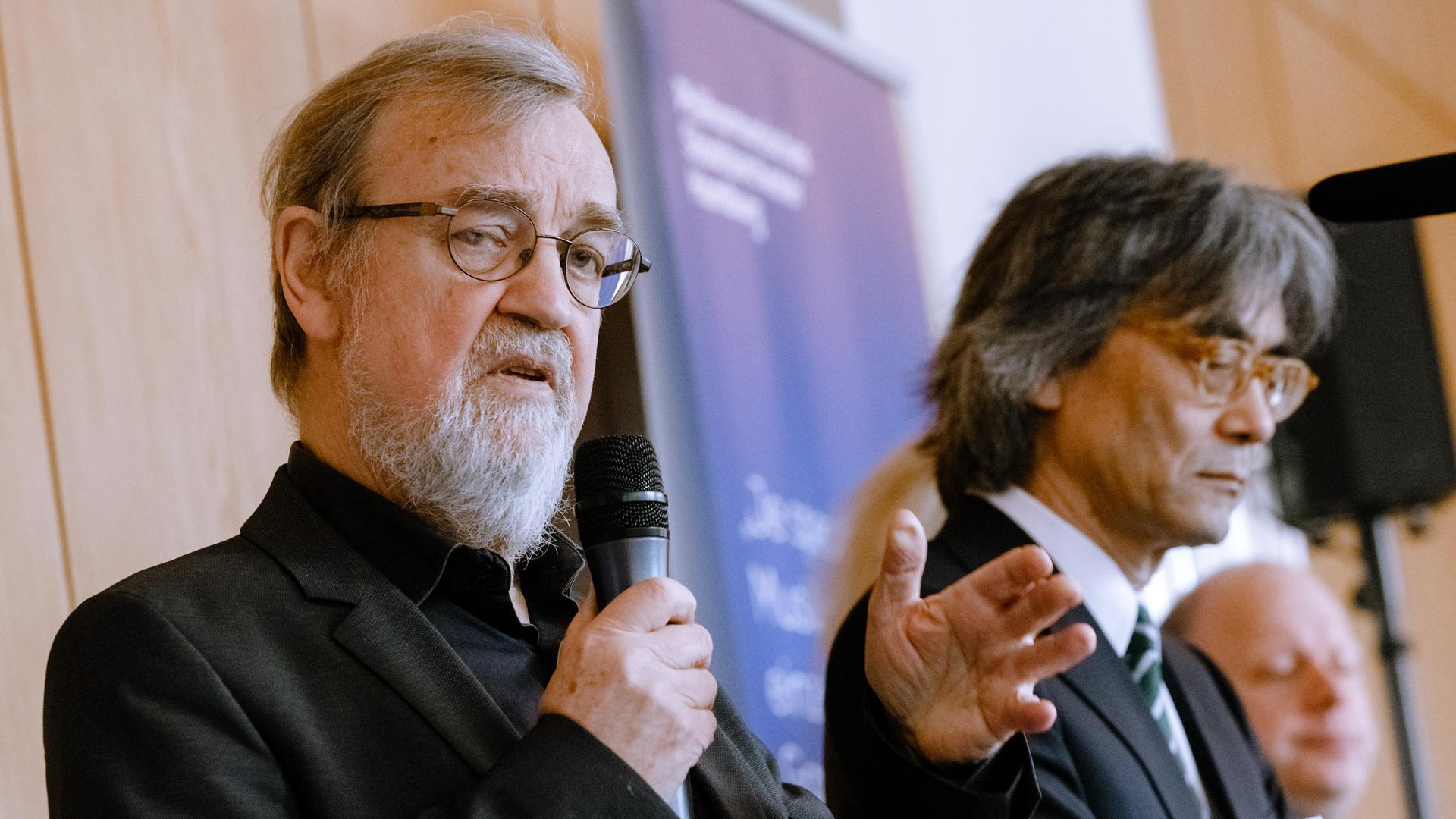 Dieter Rexroth (links) mit einem Mikrophon in der Hand neben Kent Nagano bei einer Presskonferenz