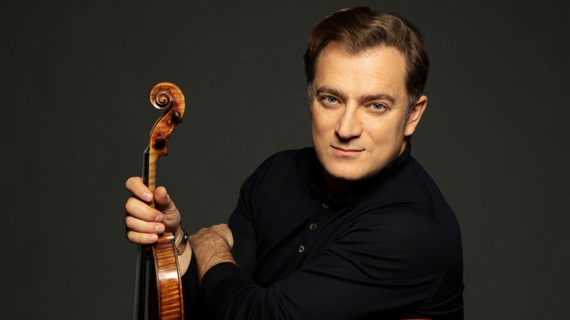 Renaud Capuçon schaut über seine linke Schulter in die Kamera, während er seine Violine präsentiert.