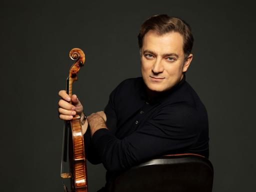 Renaud Capuçon schaut über seine linke Schulter in die Kamera, während er seine Violine präsentiert.