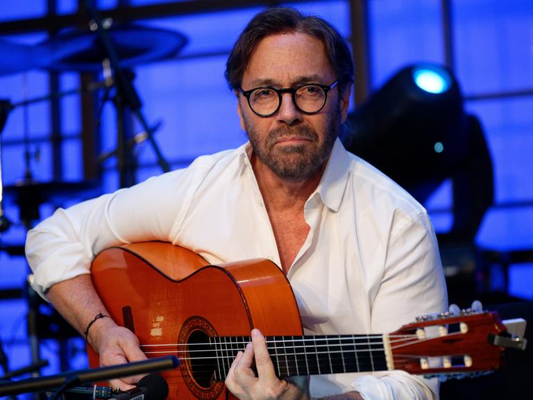 Der Musiker Al Di Meola sitzt mit einer Gitarre auf der Bühne.