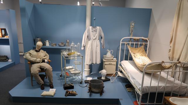 Ausstellungsraum: Ein Krankenzimmer aus dem vorigen Jahrhundert, man sieht ein krankenbett und medizinische Utensilien, eine Schwesternuniform und eine Puppe in Erwachsenengröße, die auf einem Stuhl sitzt