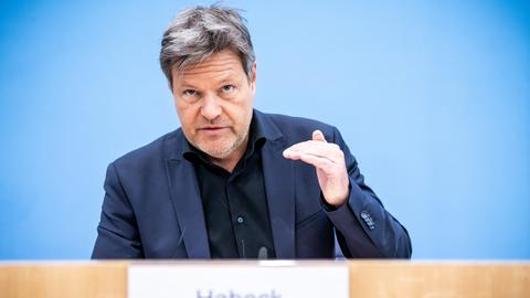 Robert Habeck sitzt in der Bundespressekonferenz und gestikuliert mit seiner linken Hand. Im Hintergrund ist die für diesen Saal typische blaue Wandfarbe zu sehen.