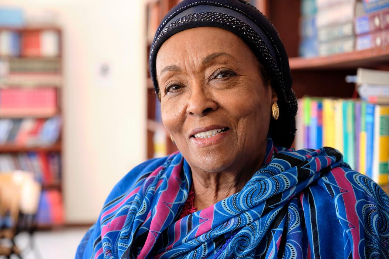 Edna Adan sitzt in einer Bibliothek vor Bücherwänden in der Hauptstadt Hargeisa. Sie trägt ein leuchtend blaues Gewand.