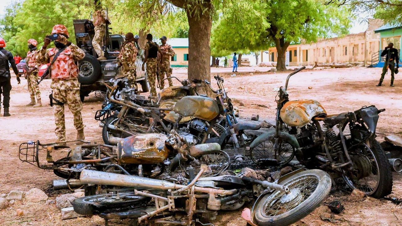 Auf einem Platz liegen mehrere verbrannte Motorrräder. Dahinter stehen mehrere Soldaten in Tarnuniformen. Auf einem Platz liegen mehrere verbrannte Motorrräder. Dahinter stehen mehrere Soldaten in Tarnuniformen.