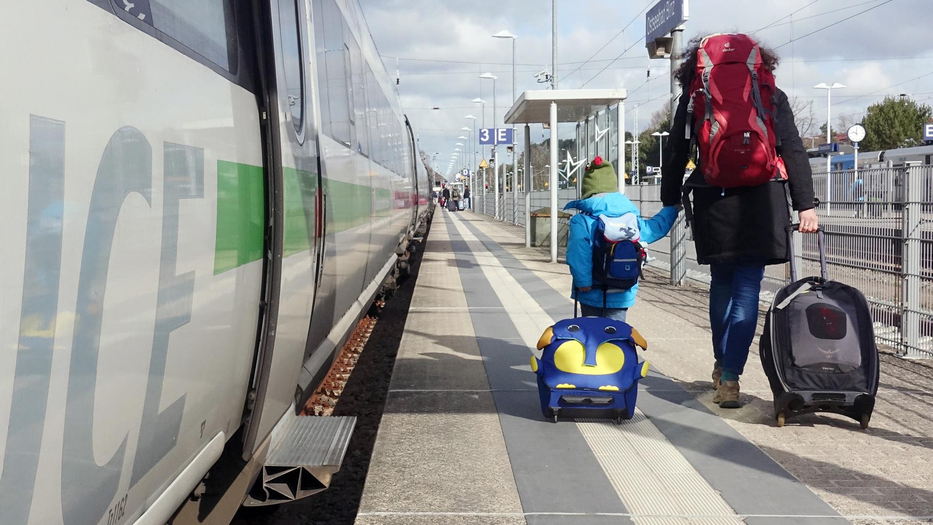 Mutter und Kind gehen auf der Suche nach ihrem ICE-Abteil den Bahnsteig am Bahnhof Binz (Mecklenburg-Vorpommern) entlang. Beide tragen Rucksäcke, die Frau hat ihr kleines Kind an die Hand genommen.