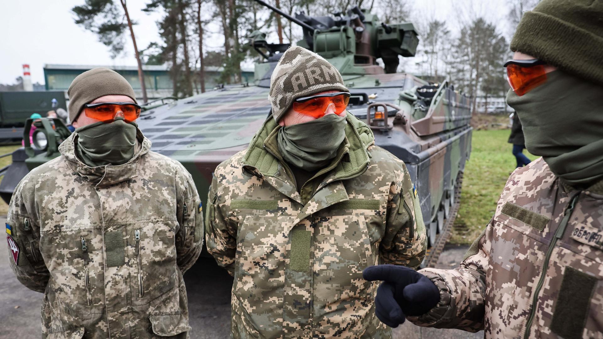 Zu sehen sind drei ukrainische Soldaten vor einem Schützenpanzer Marder in der Panzertruppenschule im niedersächsischen Munster.