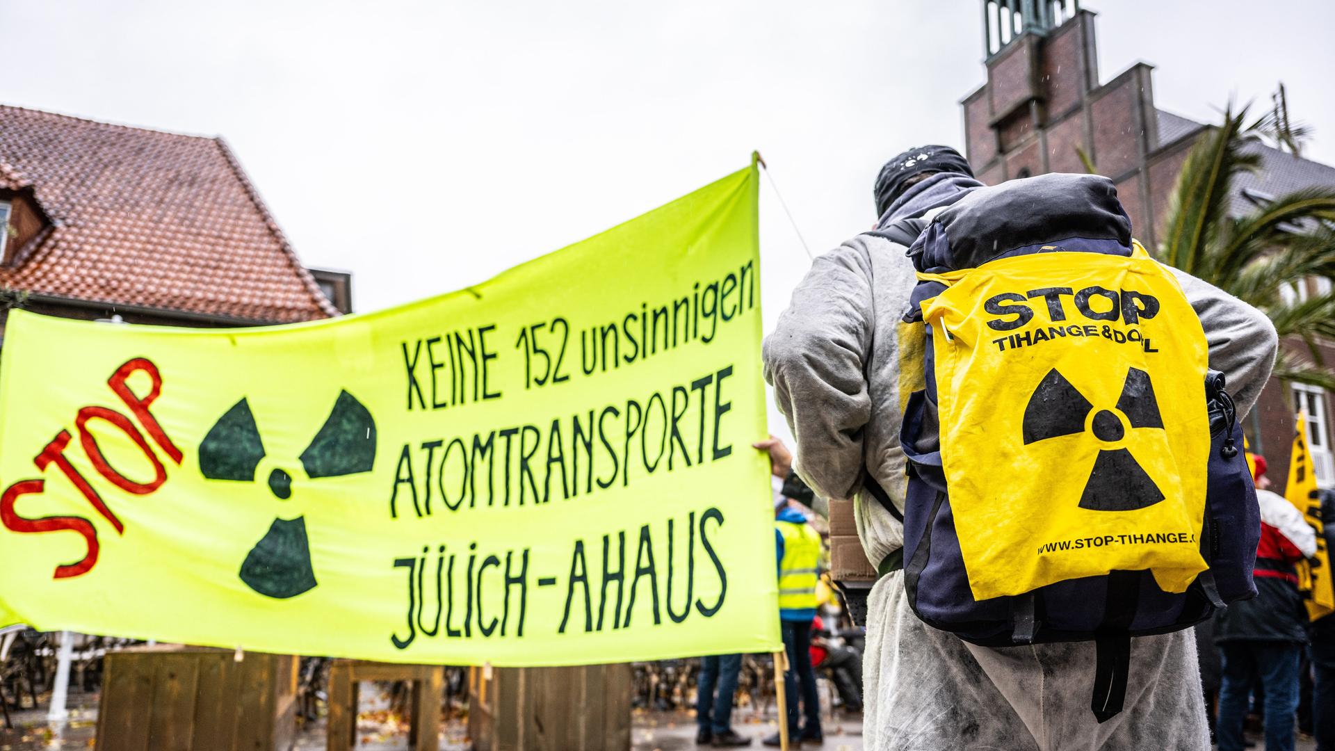 Das Bild zeigt eine Anti-Atommüll-Kundgebung in Ahaus. Zu sehen ist ein Transparent mit der Aufschrift: "Keine 152 unsinnigen Atomtransporte Jülich-Ahaus". Eine Person trägt auf dem Rücken einen Jute-Beutel gegen Atommüll.