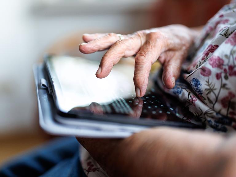 Eine 95-jährige Dame bedient ihr Tablet und schreibt eine Nachricht in einem Messenger.