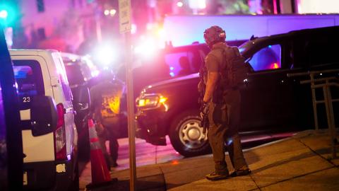 Einsatzkräfte mit militärischer Ausrüstung stehen nachts auf einer grell ausgeleuchteten Straße und sichern die Gegend