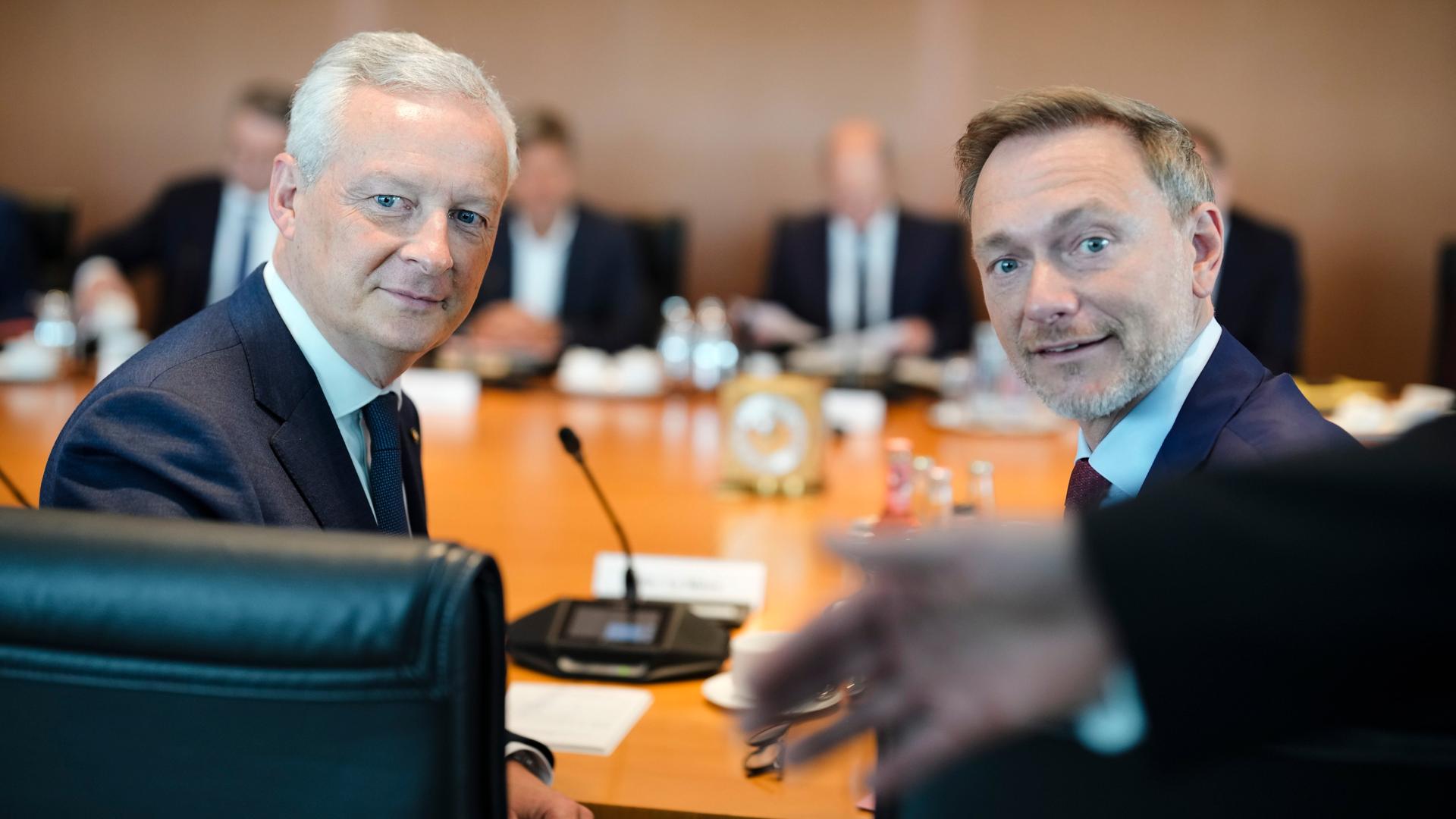 Der französische Wirtschafts- und Finanzminister Bruno Le Maire sitzt mit dem deutschen Finanzminister Christian Lindner nebeneinander an einem Tisch. Hinter ihnen auf der Tischplatte steht ein Mikrofon.