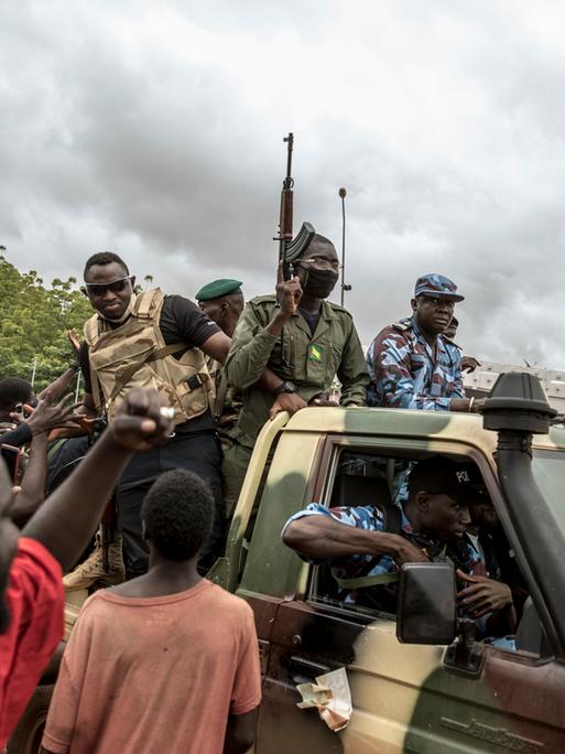 Menschen jubeln, während Sicherheitskräfte durch die Straßen der Hauptstadt Bamako in Mali fahren, 2020. Der Putsch hat den malischen Präsidenten von der Macht vertrieben.