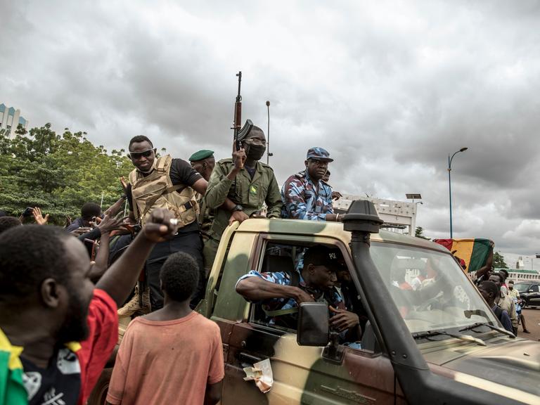 Menschen jubeln, während Sicherheitskräfte durch die Straßen der Hauptstadt Bamako in Mali fahren, 2020. Der Putsch hat den malischen Präsidenten von der Macht vertrieben.