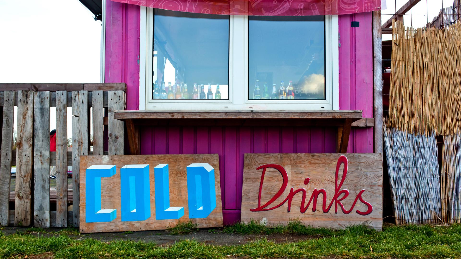 Schilder mit der Aufschrift "Cold" und "Drinks" stehen vor einem Container, der zur Bar umfunktioniert wurde.