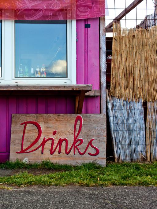 Schilder mit der Aufschrift "Cold" und "Drinks" stehen vor einem Container, der zur Bar umfunktioniert wurde.