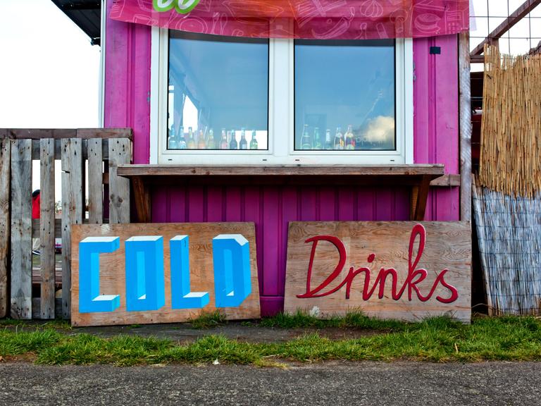 Schilder mit der Aufschrift "Cold" und "Drinks" stehen vor einem Container, der zur Bar umfunktioniert wurde.