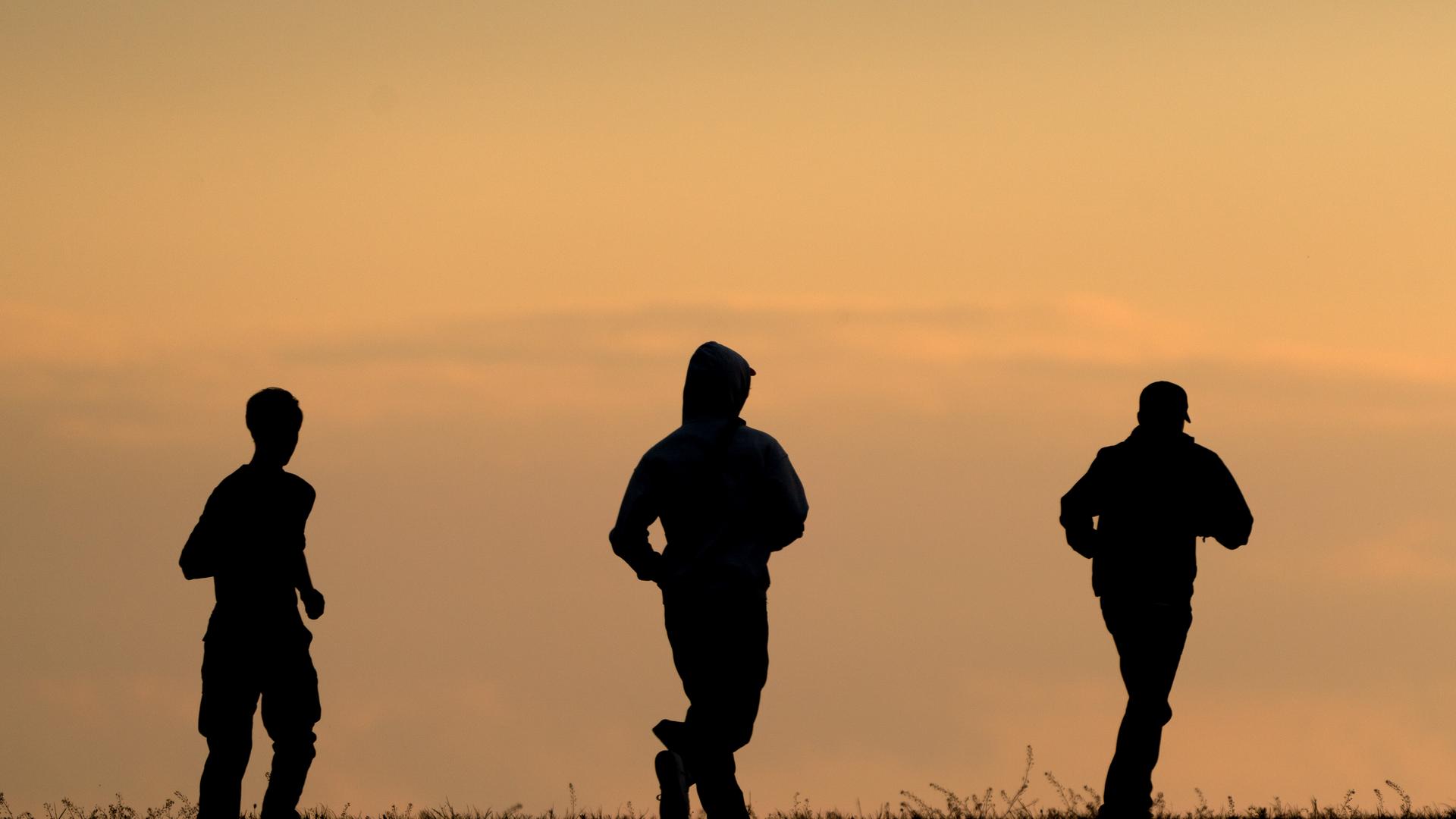 Drei junge Männer laufen auf dem Drachenberg im Westen der Stadt dem Sonnenuntergang entgegen.