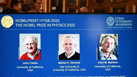Stockholm: Standbild aus dem Livestream zur Bekanntgabe des Nobelpreises für Physik 2025: Auf einer Leinwand ist die Präsentation der Preisträger, die in den USA forschenden Quantenphysiker John Clarke (l-r), Michel Devoret und John Martinis, zu sehen.