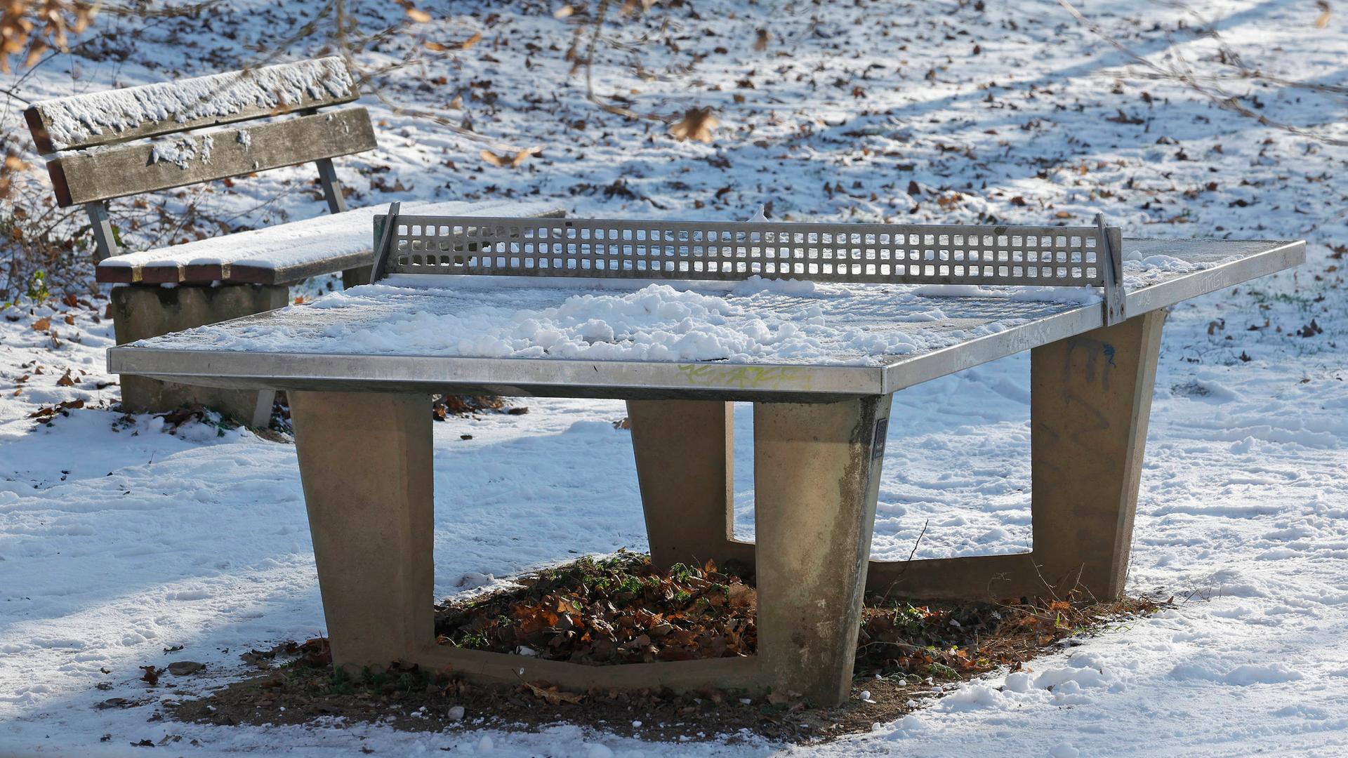 Eine verschneite Tischtennisplatte im Winter in einem Park. 